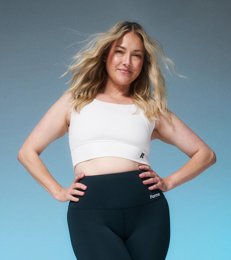 Woman in a white Collagen Power Bra and dark leggings, hands on hips