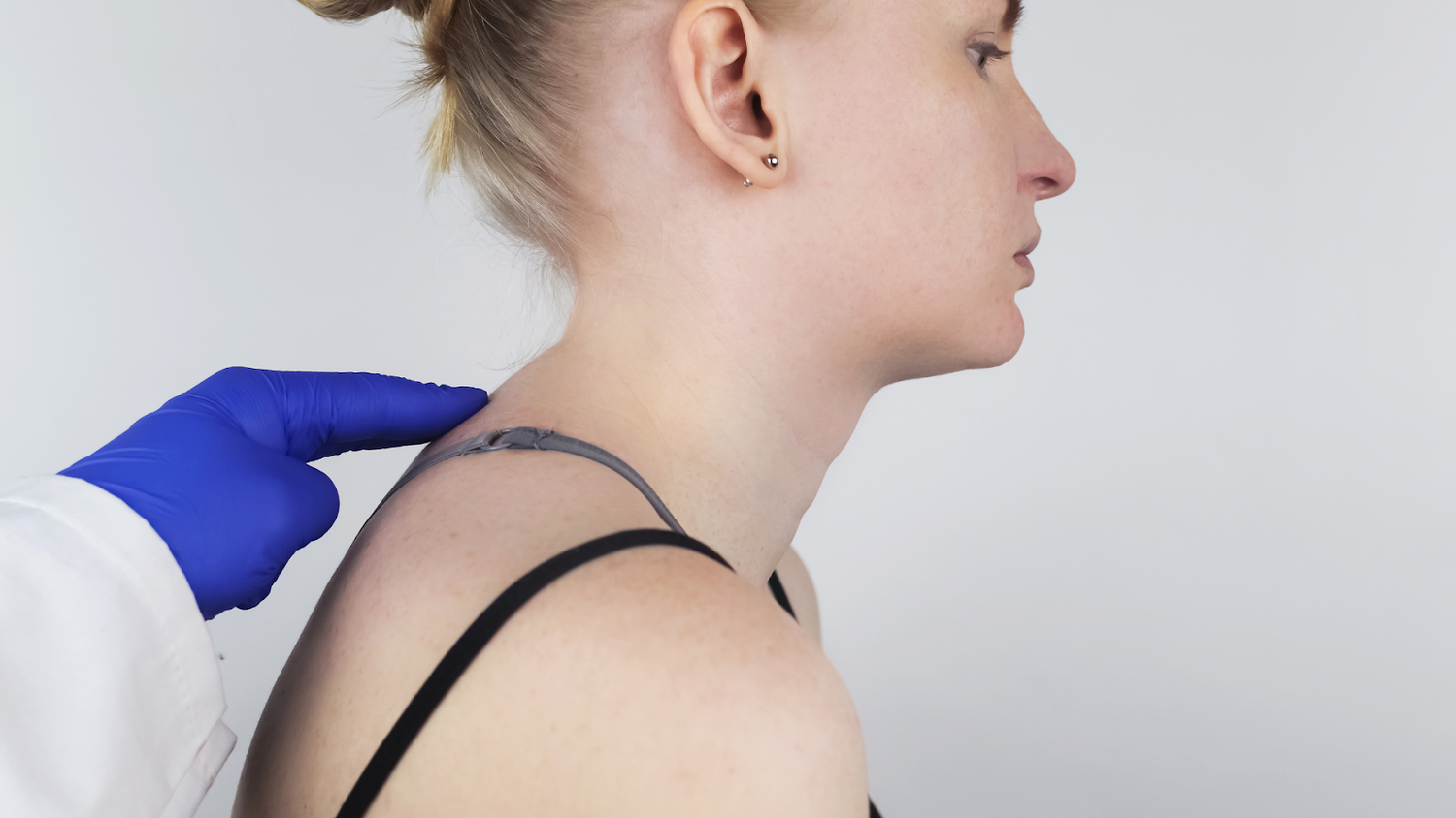 Gloved Hand Points To Tech Neck Hump On Woman's Upper Back