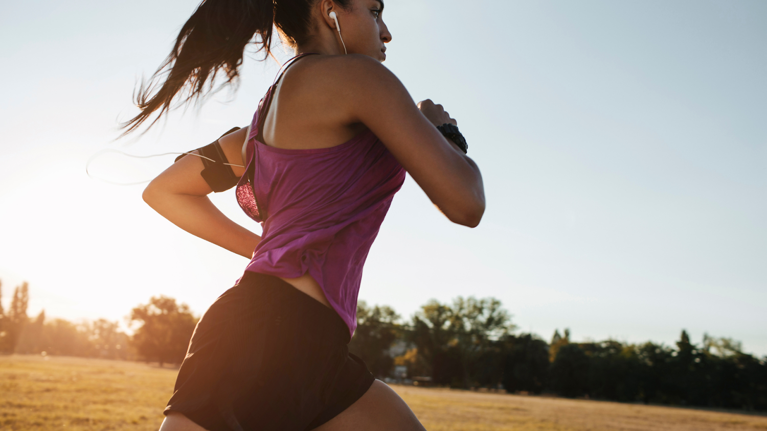 Woman running outdoors at sunset in a purple tank top