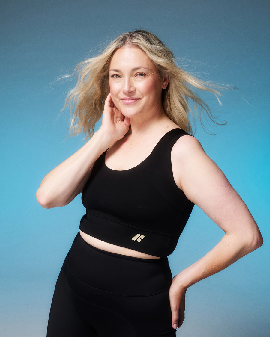Woman smiling in the Collagen Power Bra against a blue backdrop