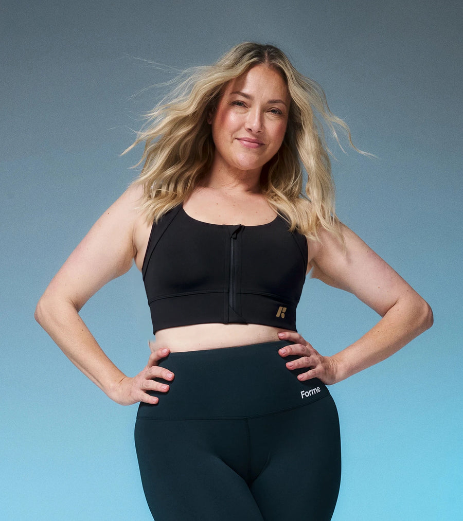 Woman in a white Collagen Power Bra and dark leggings, hands on hips